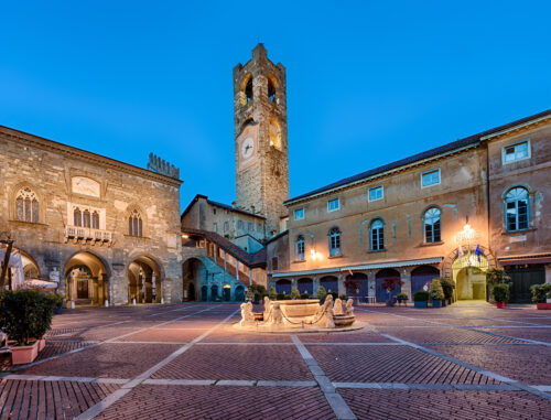 A view at dusk of Bergamo's old town square, with brick pavements and the clocktower.