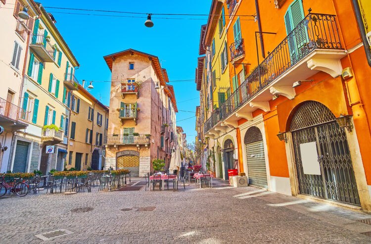The old town street in Brescia with coloured houses and outdoor cafes with chairs on the cobbles, Lombardy
