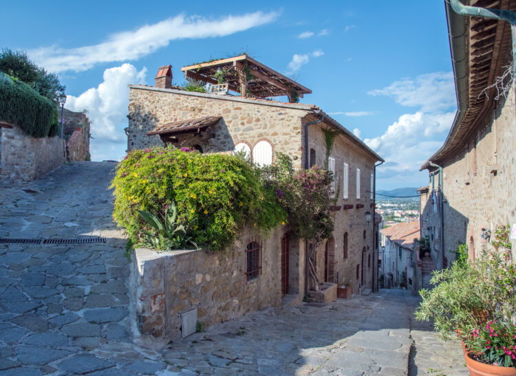 Looking along a street in Castiglione della Pescaia in Tuscany Italy on a hillside, cobbled street, with a view in the background.
