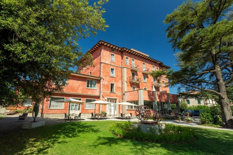 View of the Grand Hotel Impero from the grounds, between the trees on a sunny day, showing the outside terrace area where meals and drinks can be taken.
