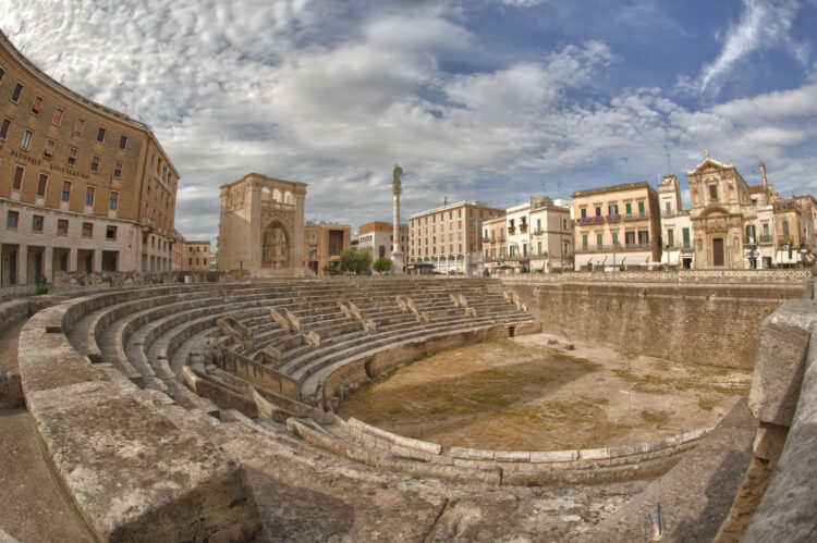 A view of the amphitheatre in Lecce town, Italy showing the stone seats, with the town's buildings surrounding it.