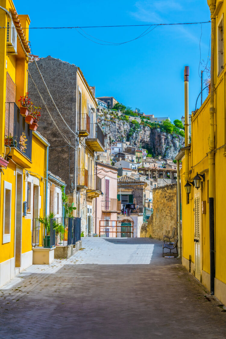 View of a narrow street in Modica, Sicily, Italy with cobbled street. An authentic Italian street with a bright blue sky and yellow houses.